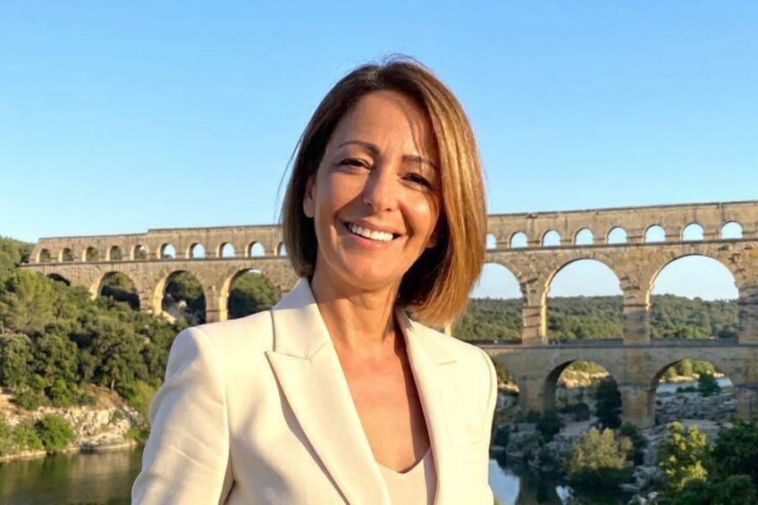 A person in front of a stone bridge with arches over a river. 1