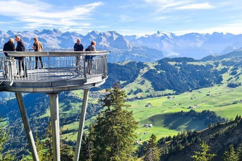 A group of people on a lookout platform overlooking a mountainous landscape with green valleys and distant peaks. 1