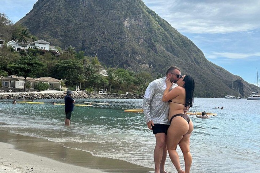A couple kissing on a beach with a mountain in the background. 3
