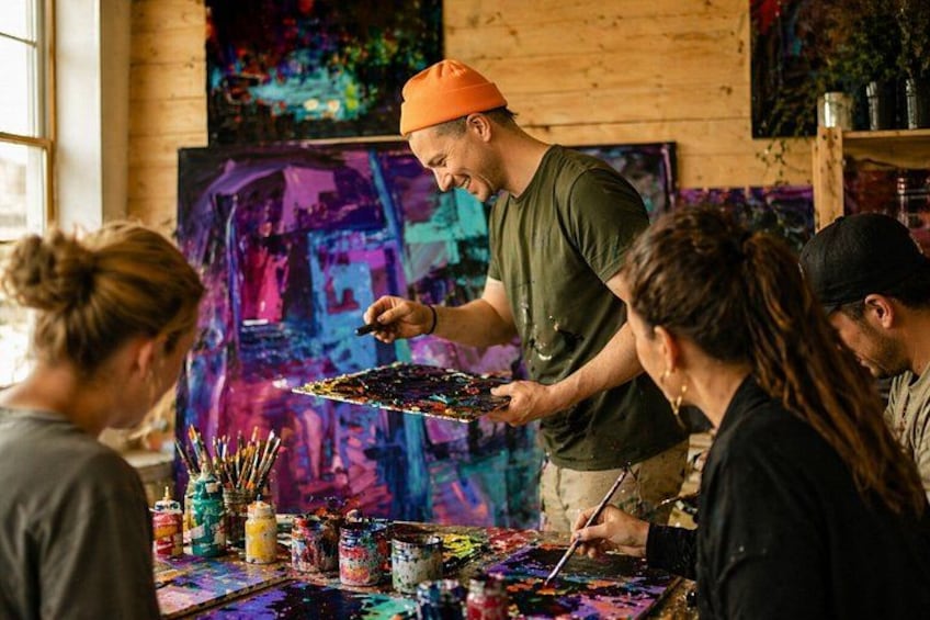 Een groep mensen die bezig is met schilderen in een kamer met houten wanden en kleurrijke kunstwerken. 1
