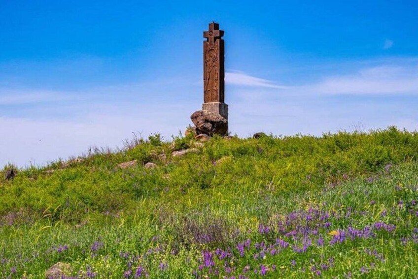A tall, weathered stone cross on a grassy hill with wildflowers. 3