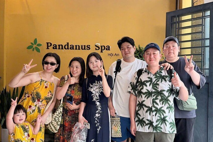En grupp människor poserar framför en byggnad med en skylt som visar texten ”Pandanus Spa”. 2