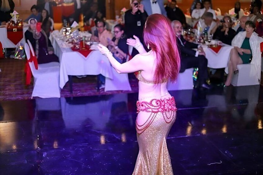 A belly dancer performing on a stage with an audience seated at tables. 4