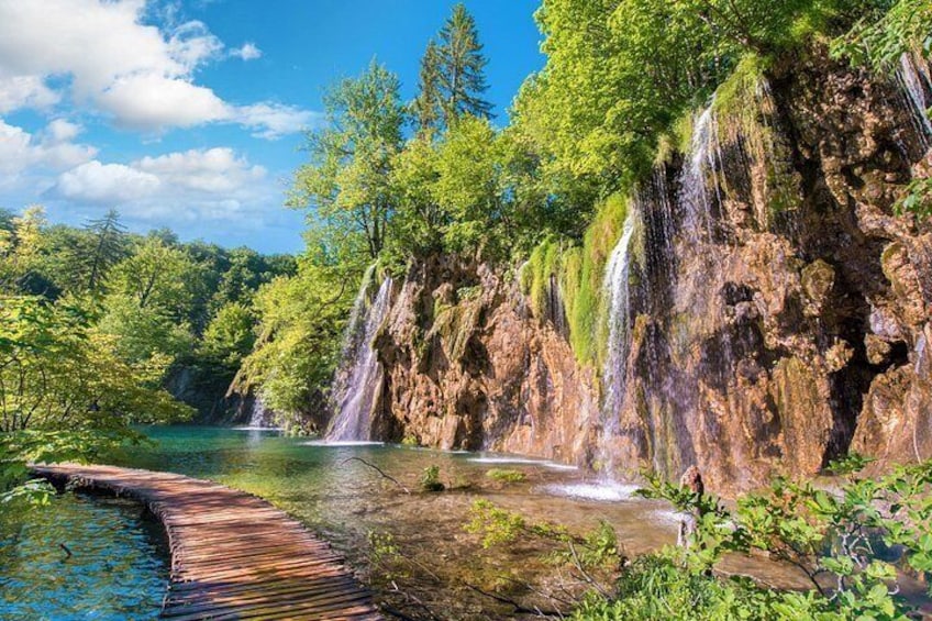 A wooden bridge over a river, a waterfall, and lush greenery. 2