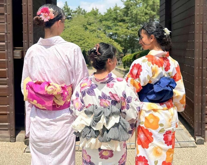 Three individuals in traditional Japanese attire standing in front of a wooden gate. 3