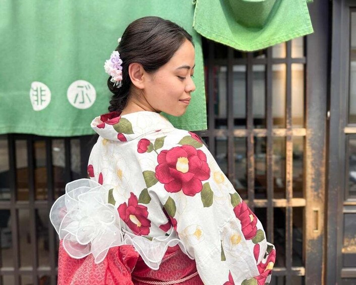 A person wearing a floral-patterned garment with a white and red color scheme, standing in front of a green backdrop with white characters. 4