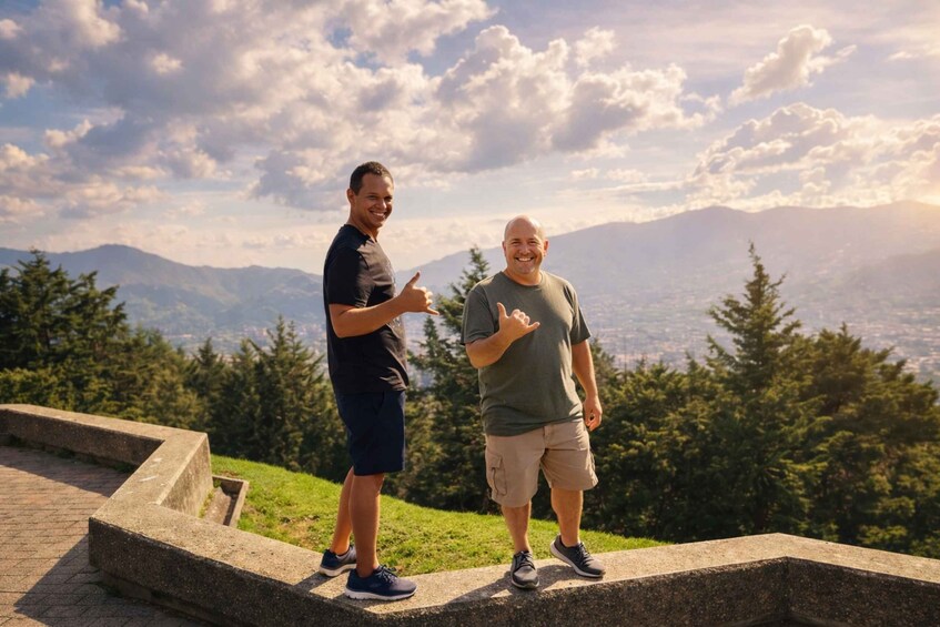 Two people standing on a stone platform with a mountainous landscape in the background. 2