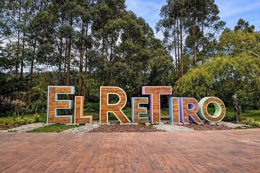 Large wooden letters spelling 'EL RETIRO' in a landscaped area with trees and a paved path. 5