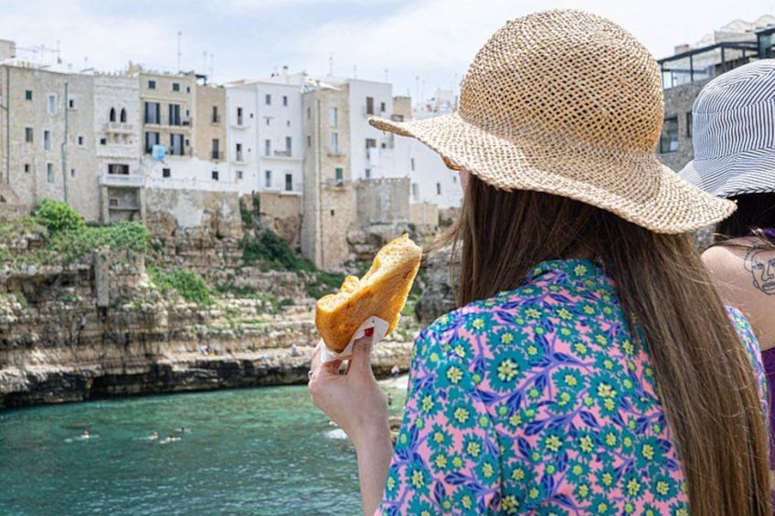 Una persona tiene un panino in prossimità della costa, con edifici sullo sfondo. 2