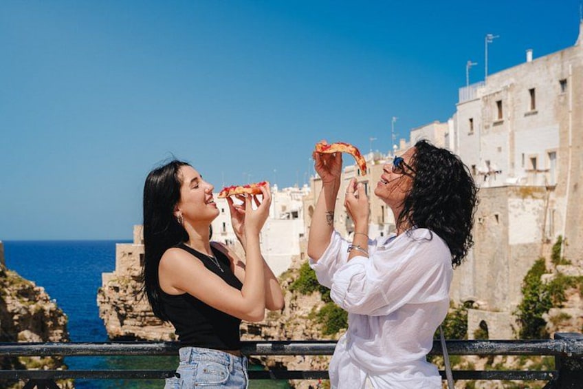 Due persone mangiano pizza su un balcone con vista sulla città costiera. 1