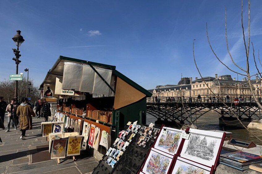 Un mercado callejero con puestos de arte, un puente y edificios históricos al fondo. 1