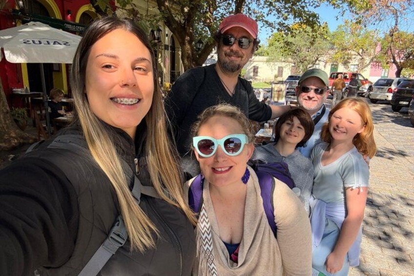 Un groupe de personnes prenant un selfie à l’extérieur, avec des arbres et un bâtiment en arrière-plan. 1