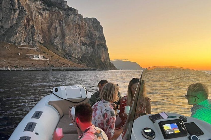 Eine Gruppe von Menschen auf einem Boot in der Nähe einer Klippe am Wasser bei Sonnenuntergang. 2