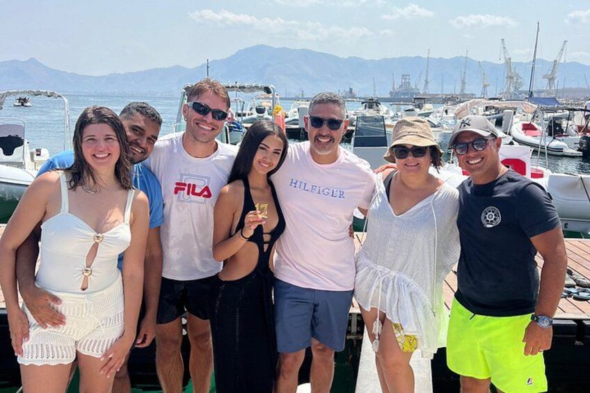 A group of people posing by a marina with boats and mountains in the background. 3