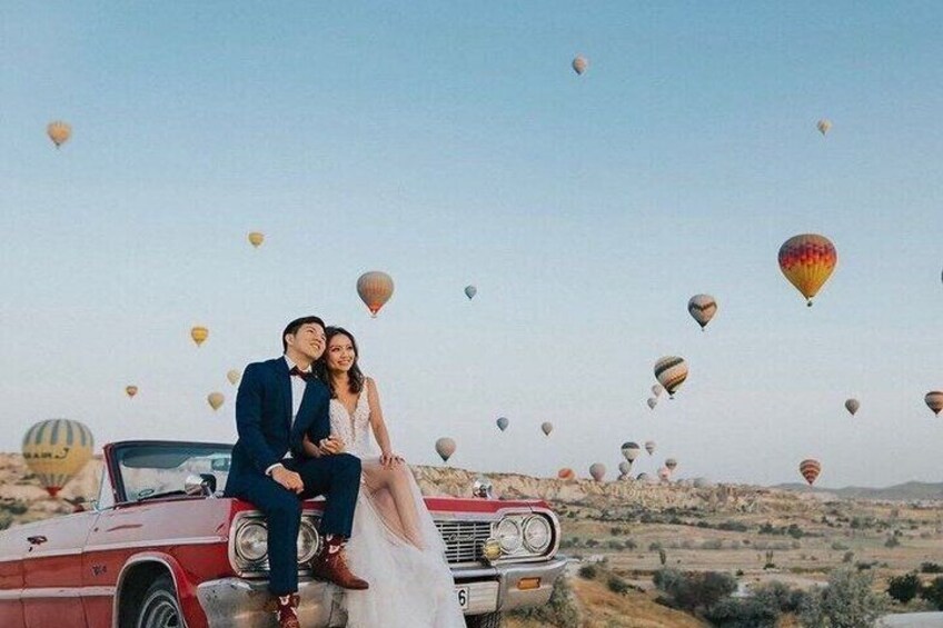 A couple on a vintage car with hot air balloons in the background. 3