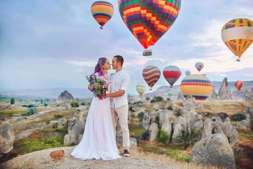 A couple embracing with a landscape of rock formations and hot air balloons in the background. 2