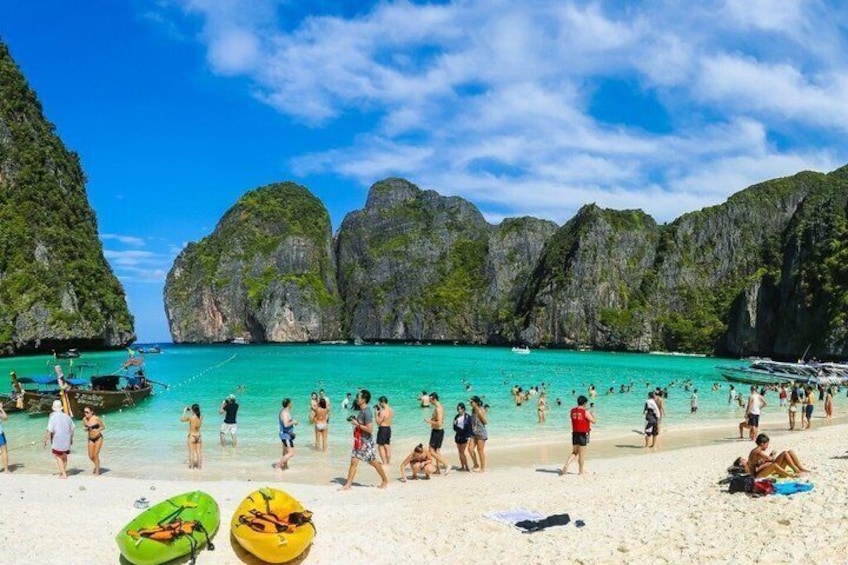 Una playa concurrida de aguas turquesas cristalinas, acantilados rocosos y gente tomando el sol. 2