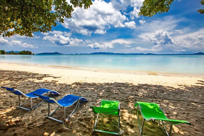 A beach with clear turquoise water, a sandy shore, and a row of blue and green lounge chairs under a partly cloudy sky. 5