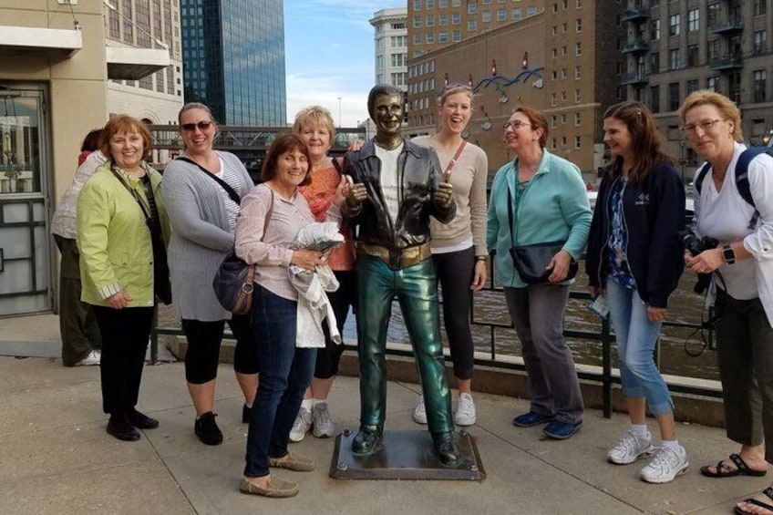 A group of people standing around a statue in an urban setting with buildings in the background. 5