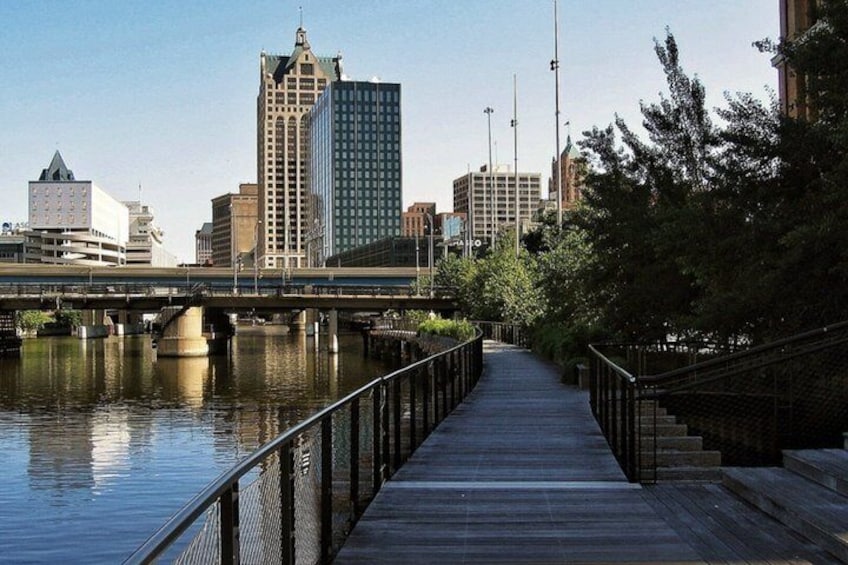 A riverside walkway with a bridge, city buildings, and a wooden deck. 3