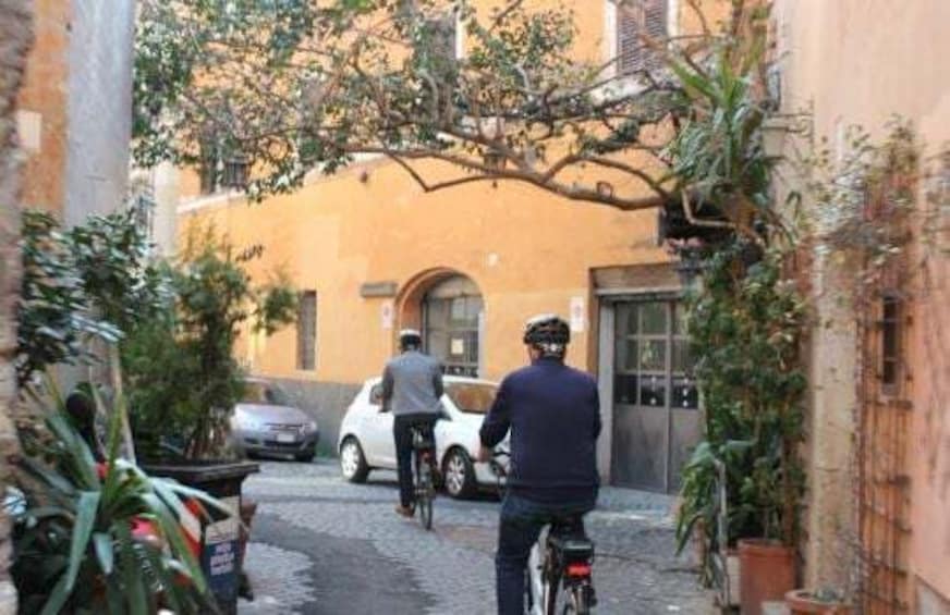 A narrow alley with a cyclist, a parked car, and a building with a yellow facade. 5