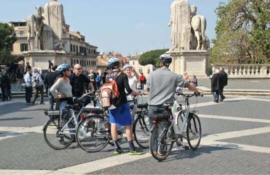 A group of cyclists gathered around a statue in a public square. 1