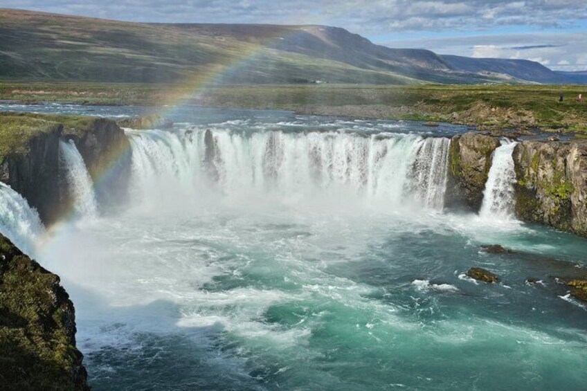 A waterfall with a rainbow, surrounded by mountains and a river. 1