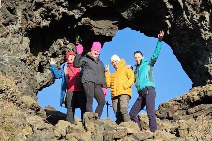 A group of people standing on rocky terrain with a large rock arch formation in the background. 2