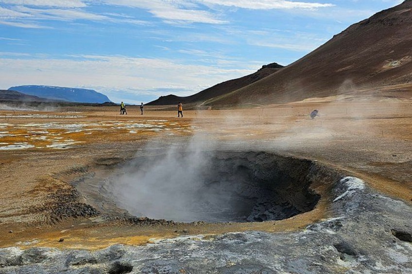 A geothermal area with steam vents, a crater, and a distant mountain range. 3