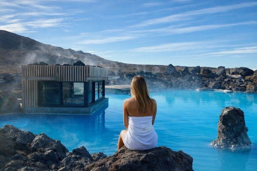 A person sitting by a geothermal pool with a wooden structure in the background. 4