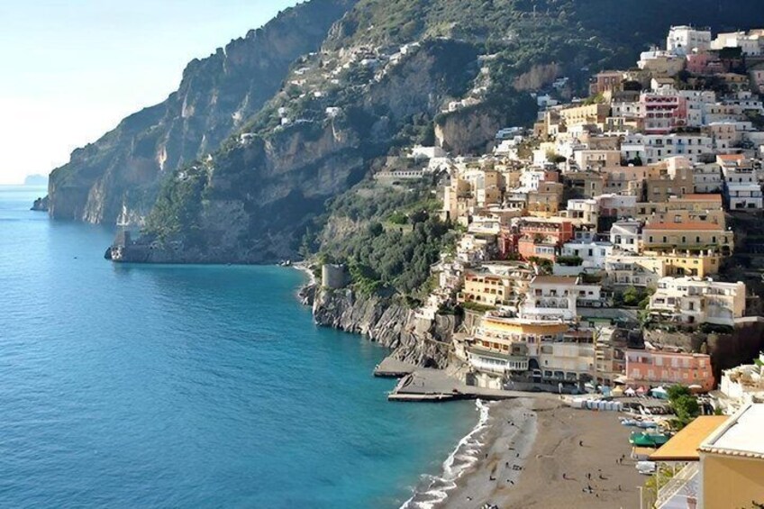 A coastal town with buildings stacked on a cliff, a beach, and a lighthouse. 1
