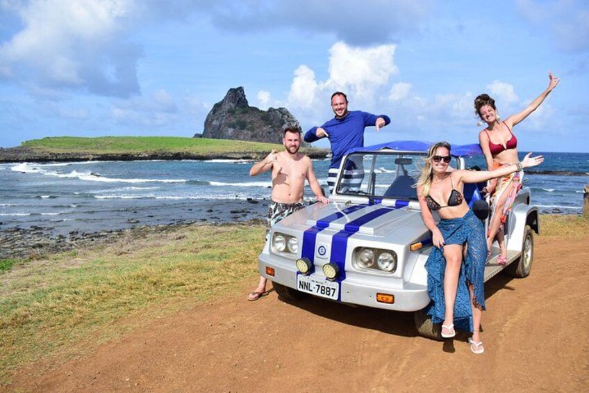 A group of people posing with a vehicle on a coastal road. 1