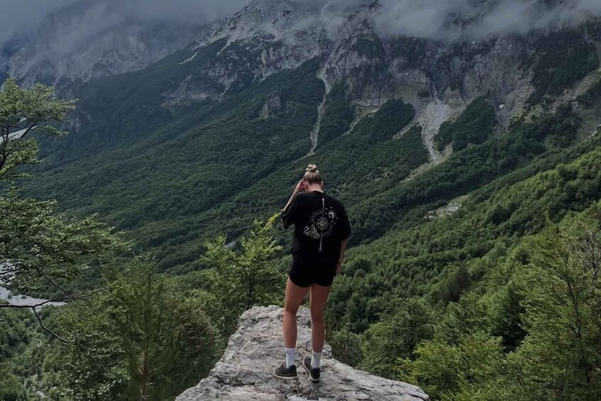 A person standing on a rock with a mountainous landscape in the background. 5