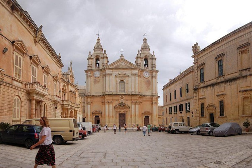 Eine historische Kirche mit zwei Türmen, einem gepflasterten Platz und abgestellten Fahrzeugen. 3