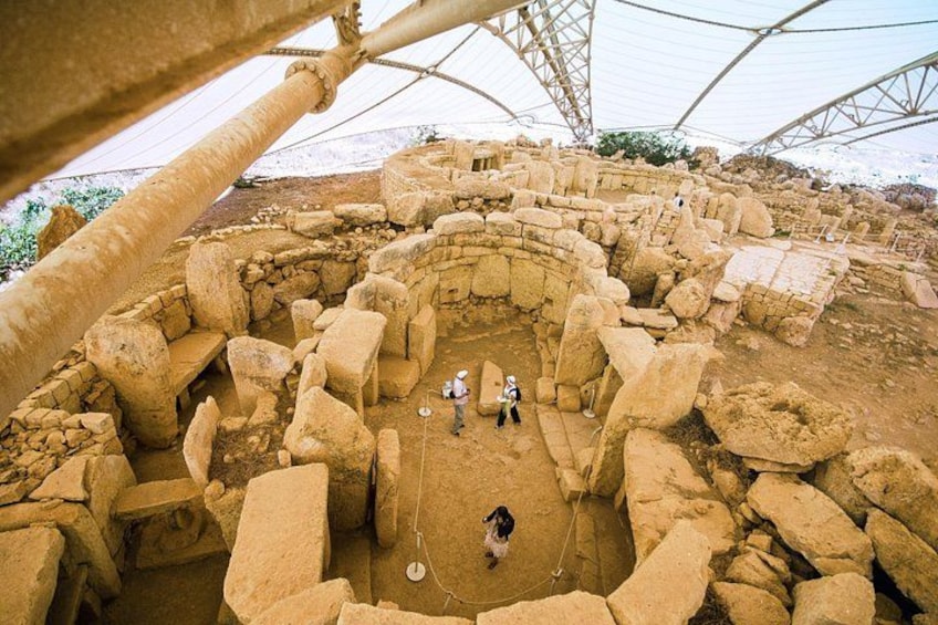 Eine archäologische Stätte mit großen Steinbauten und einer Person, die den Boden untersucht. 1