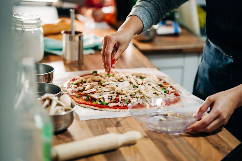 A person preparing a pizza with various toppings on a wooden table. 5