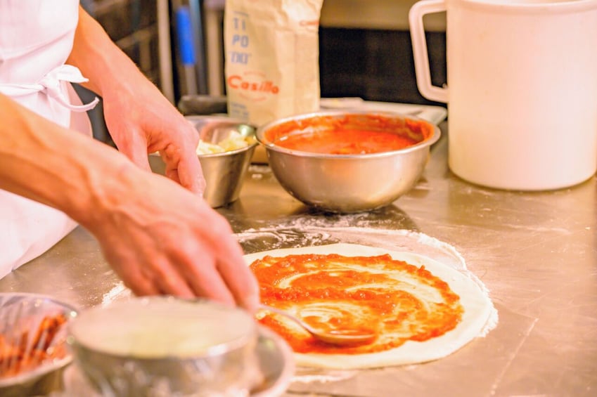 A person preparing pizza dough with tomato sauce on a kitchen counter. 4