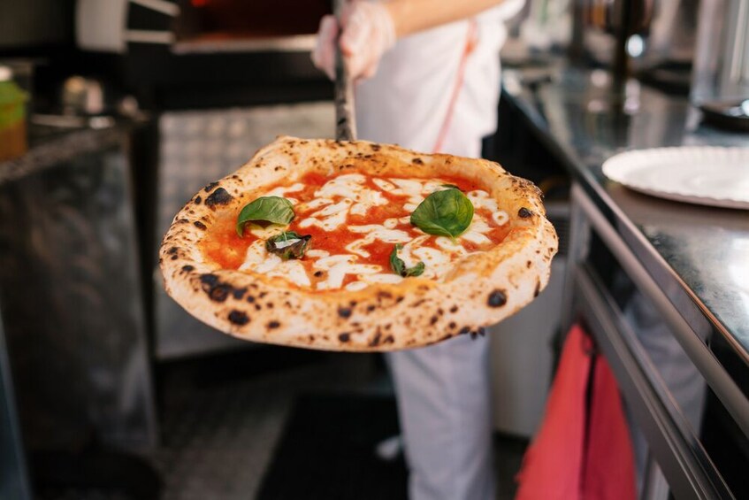 A person holding a pizza with cheese and basil leaves. 2