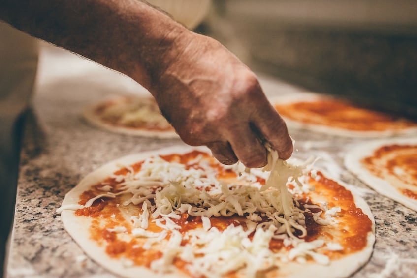 A hand sprinkling shredded cheese over a pizza dough. 3