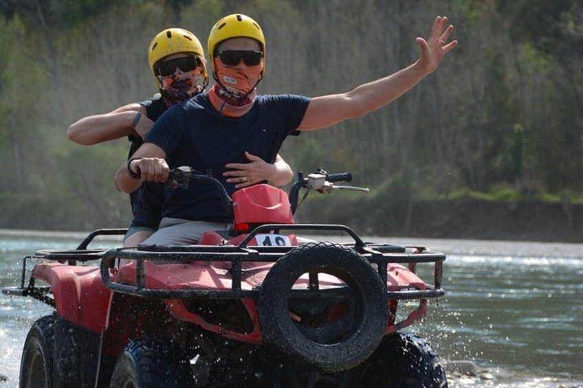 Dos personas en un cuatrimoto rojo sobre el agua, usando cascos y chalecos salvavidas. 2