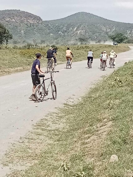 A group of cyclists on a paved road with grassy edges and hills in the background. 4