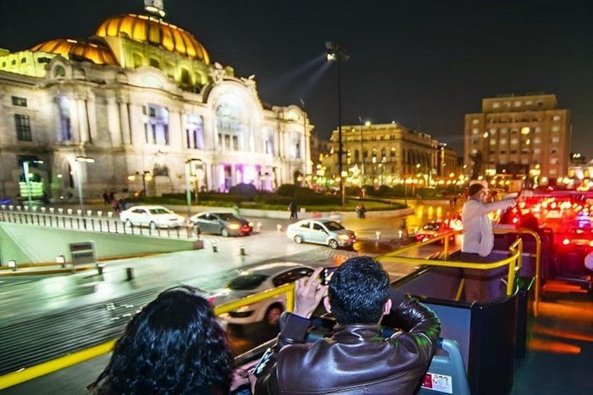 A nighttime cityscape with a large illuminated building with a dome, a busy street with cars, and a person taking a photo. 3