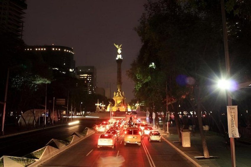 A nighttime city street with a prominent illuminated monument in the center, surrounded by traffic and urban buildings. 4