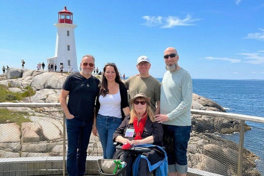 A group of people standing by a rocky coastline with a lighthouse in the background. 5
