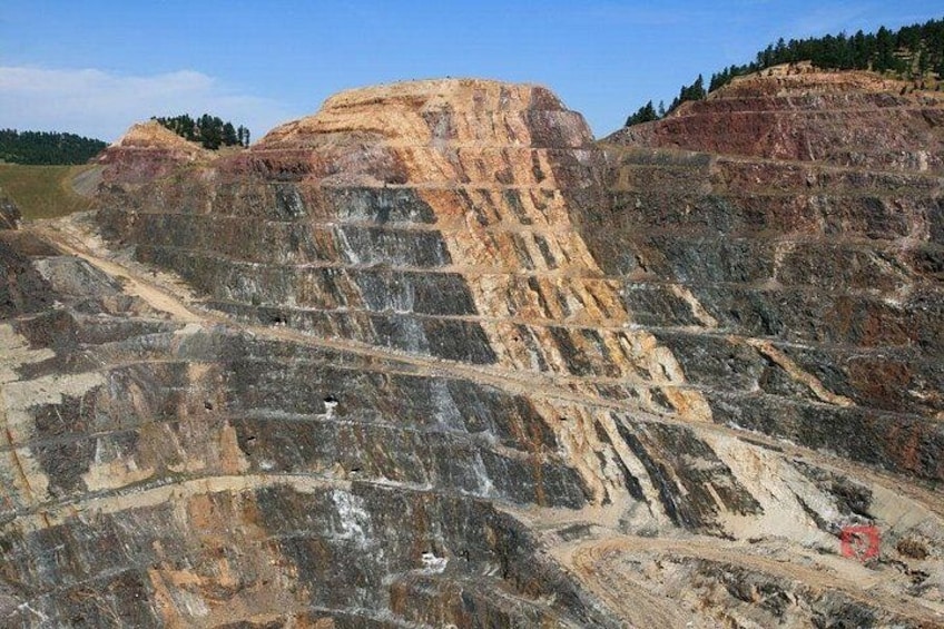 Une vaste mine à ciel ouvert, avec des formations rocheuses en strates et un petit véhicule rouge sur la droite. 5