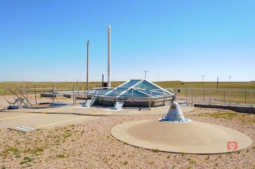 Un bâtiment moderne à la structure de verre, avec une haute tour blanche et un objet en forme de cône au premier plan. 3