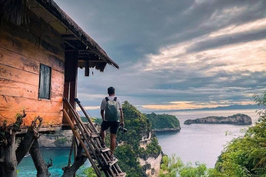 A person standing on a wooden staircase outside a house overlooking a body of water and a distant island. 5