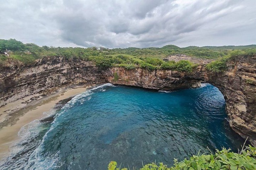 A coastal landscape with a natural rock arch, a beach, and lush greenery. 2