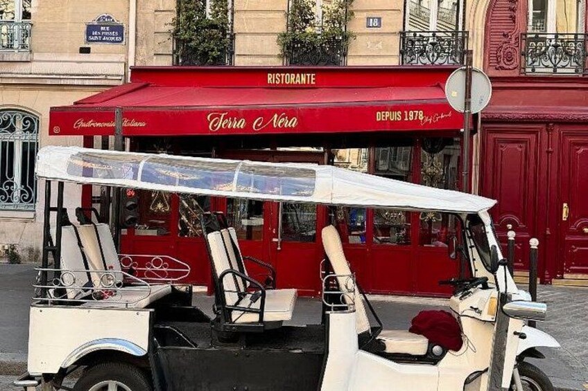 Un coche antiguo con toldo rojo, identificado con 'Terra Nera', estacionado frente a un edificio de fachada roja. 1