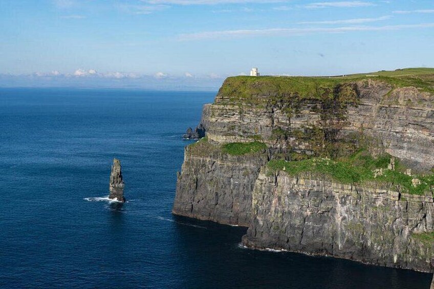 A coastal cliff with a lighthouse, a prominent rock formation in the water, and a grassy hill. 5